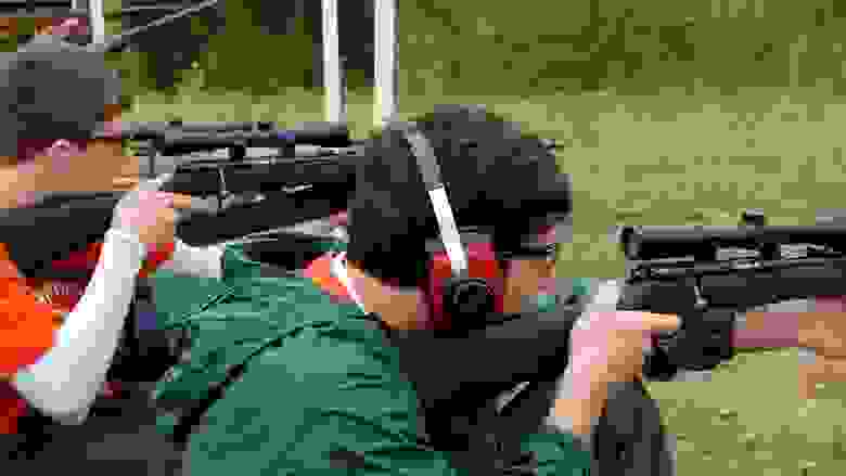 Young men wearing ear protection shooting scoped rifles at a range.