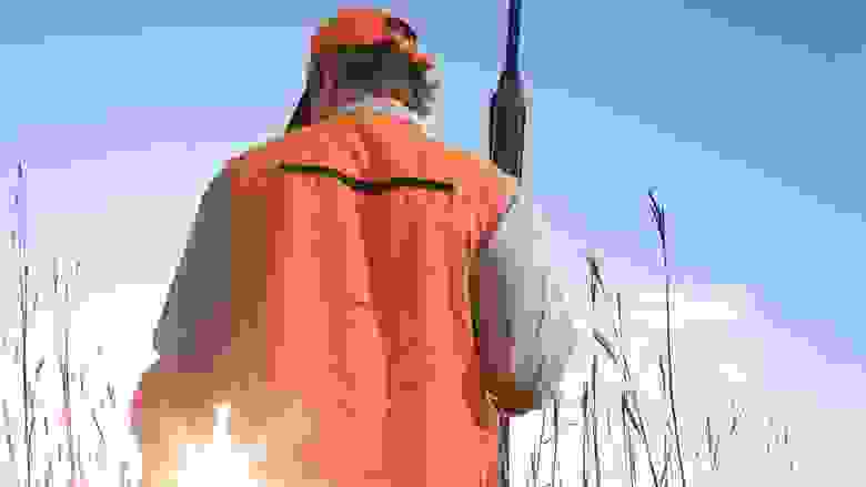Back of a hunter in blaze orange holding a shotgun with the sun in the background